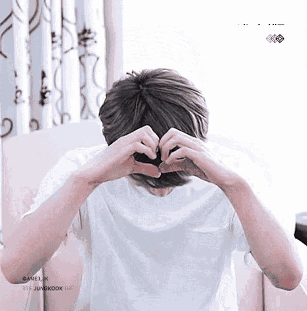 a man is making a heart shape with his hands in front of his face .
