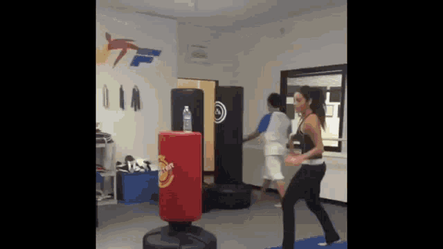 a woman is kicking a punching bag in a gym while a man watches .