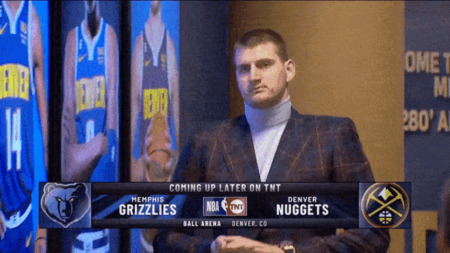 a man in a suit stands in front of a screen that says denver nuggets on it