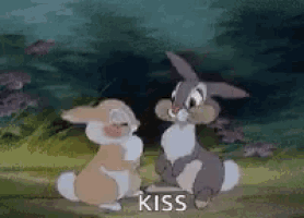 two rabbits are sitting next to each other in a forest and kissing .