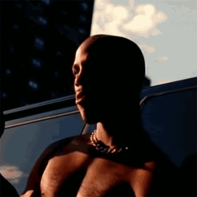 a shirtless man wearing a chain around his neck is sitting in the back seat of a car .