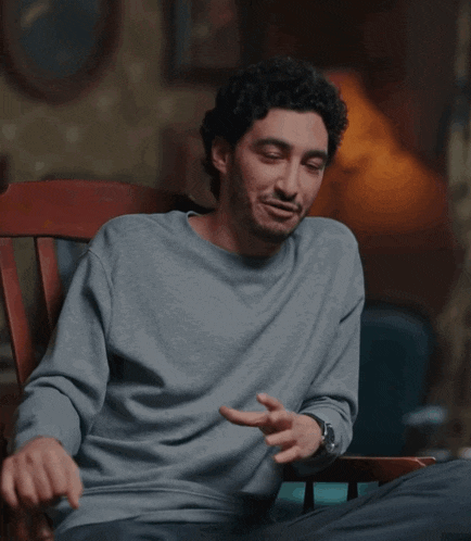 a man in a grey shirt is sitting in a chair and smiling