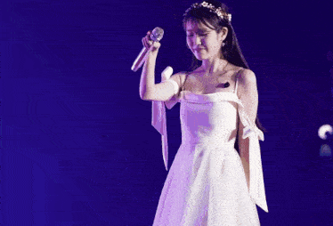 a woman in a white dress is holding a microphone in her hand