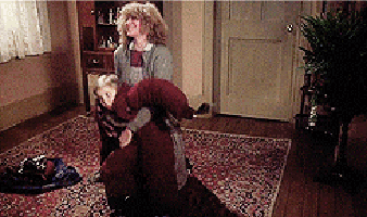 two women are fighting in a living room with a rug on the floor .