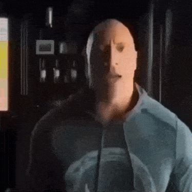 a bald man wearing a blue sweatshirt is standing in a dark room .