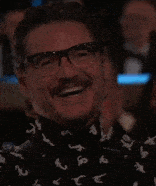 a man with glasses and a beard is wearing a shirt with letters on it