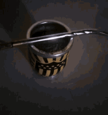 a metal cup with a straw in it and a black and yellow design on it