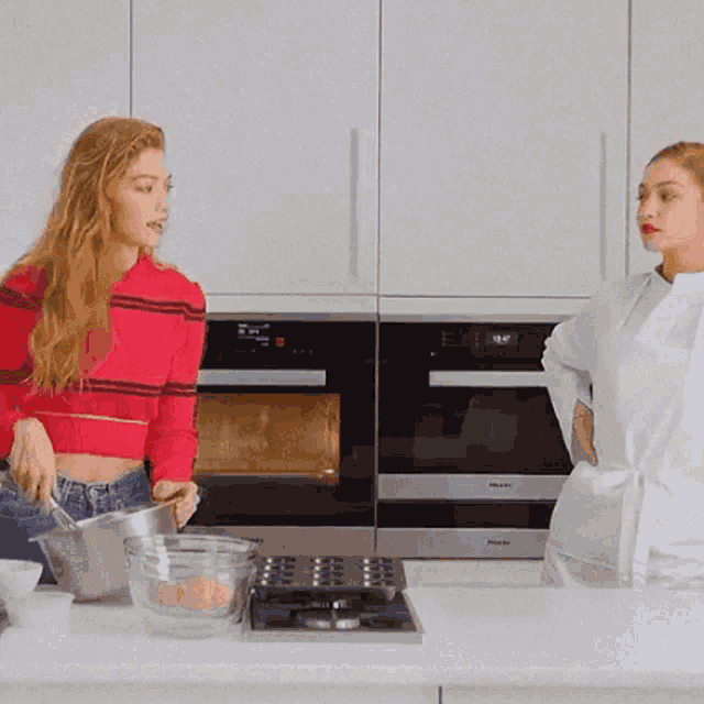 a woman in a red sweater stands next to a woman in a white apron in a kitchen