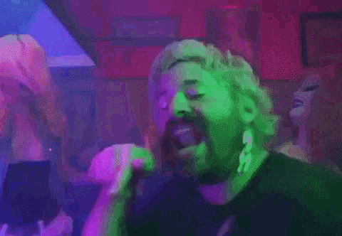 a man with a beard is smoking a cigarette in a dark room with purple and green lights .