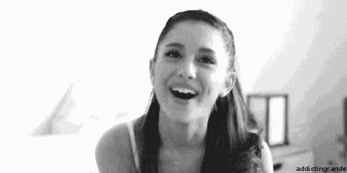 ariana grande is smiling in a black and white photo while sitting on a bed .
