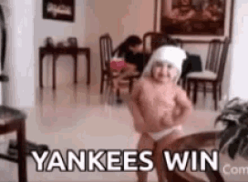 a baby is dancing in a living room with the words yankees win written on the bottom .