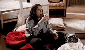 a man with long hair is sitting on the floor drinking a cup of coffee