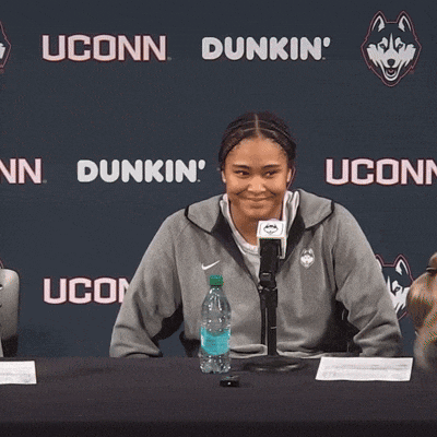 a woman sits at a table in front of a wall that says dunkin uconn