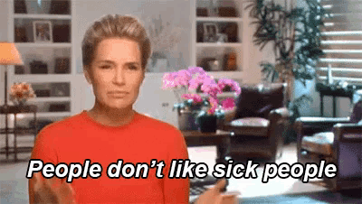 a woman in a red shirt is standing in a living room and saying `` people don 't like sick people ''