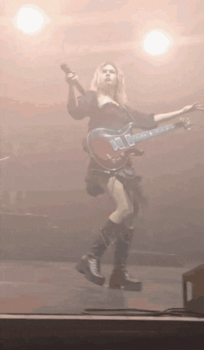 a woman is playing a guitar and singing into a microphone while dancing on a stage .