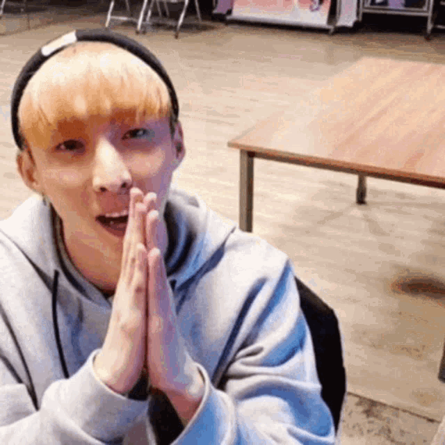 a young man with blonde hair is sitting in front of a table with his hands folded in prayer