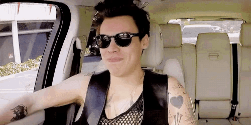 a man wearing sunglasses and a fishnet tank top is sitting in a car .