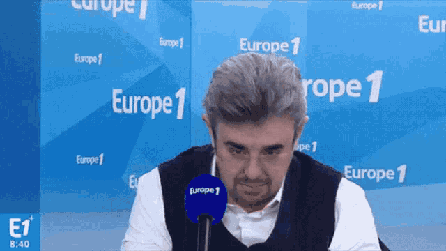a man sitting in front of a europe 1 sign