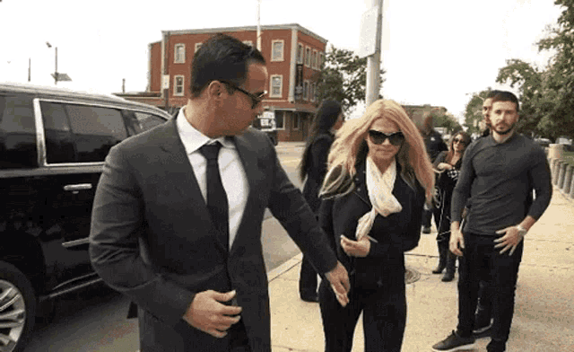 a man in a suit and tie is helping a woman walk down a sidewalk