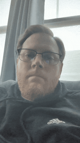 a man wearing glasses and a black adidas hoodie