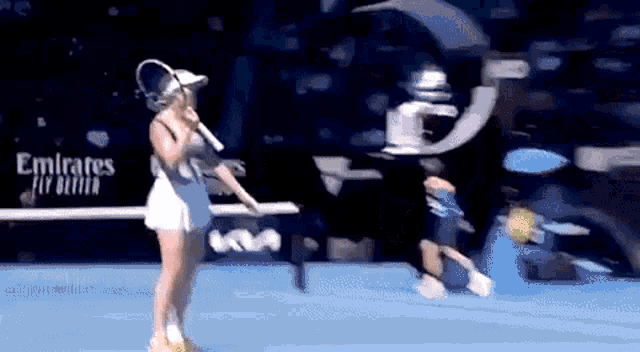 a woman in a white dress is holding a tennis racquet on a blue court .