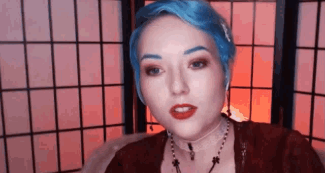 a woman with blue hair and red lipstick is wearing a choker necklace and earrings .