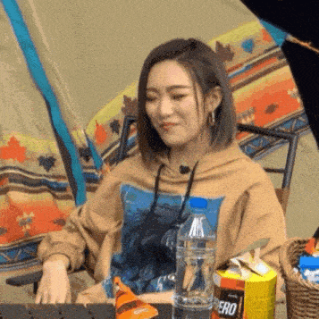 a woman is sitting in a chair in front of a tent with a bottle of water and a bag of chips .