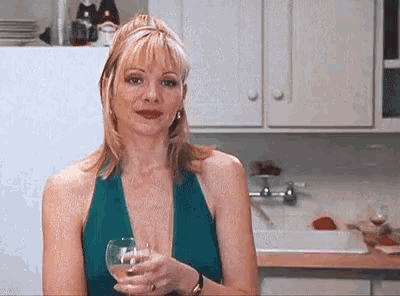 a woman in a blue dress is holding a glass of wine in a kitchen .