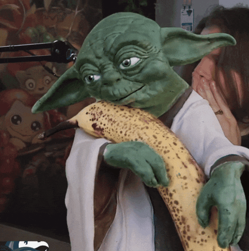 a woman is holding a green puppet that looks like yoda and a banana
