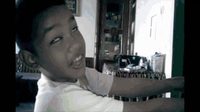 a young boy in a white shirt is smiling in a living room