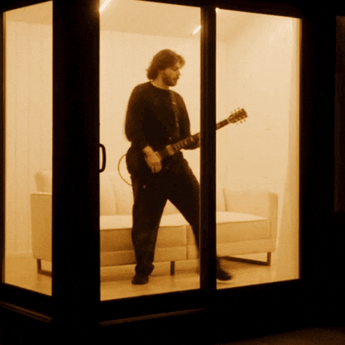 a man playing a guitar in a room with a couch