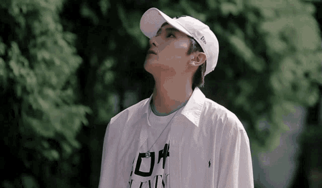 a young man wearing a white hat and a white shirt is standing in front of trees .
