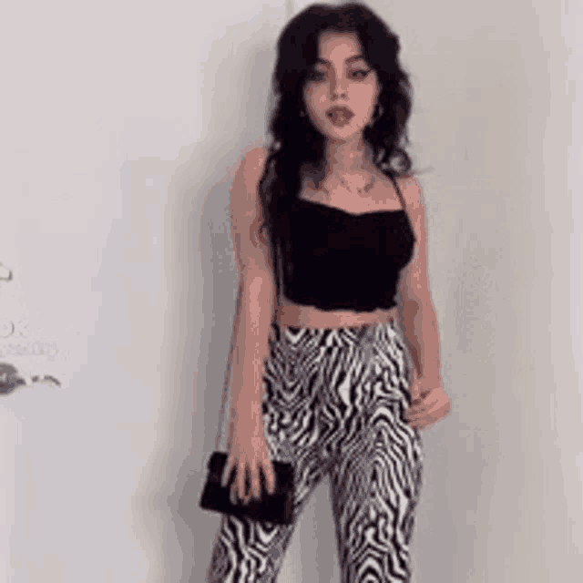 a woman in a black crop top and zebra print pants is standing in front of a white wall .