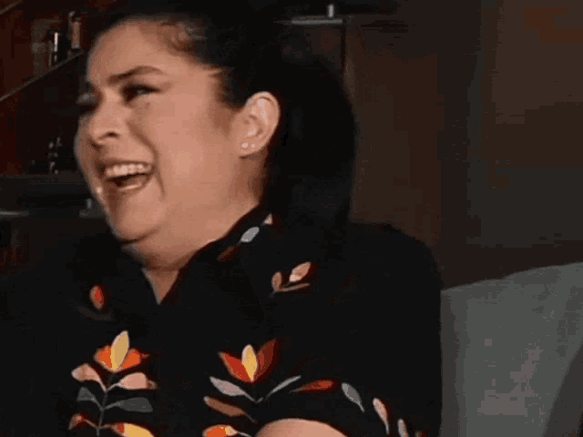 a woman is laughing with her mouth open and wearing a black shirt with flowers on it