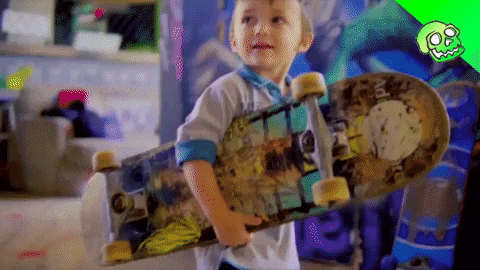 a young boy is holding a skateboard in front of a wall with graffiti