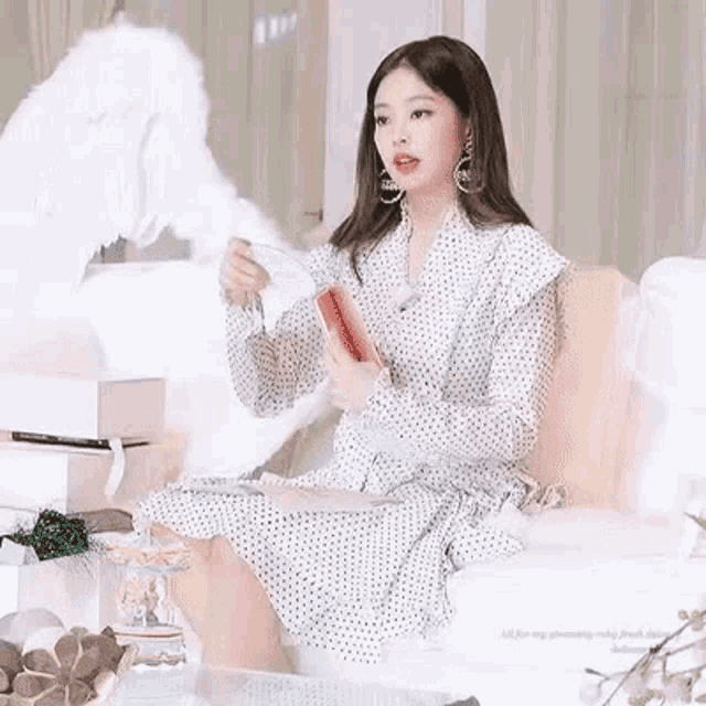 a woman in a polka dot dress is sitting on a couch holding a box and a cup .