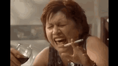 a woman is drinking wine and smoking a cigarette while holding a glass of wine .