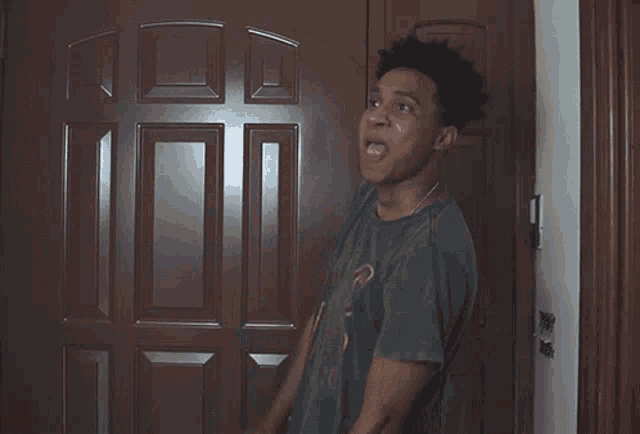 a man wearing a elvis live shirt stands in front of a brown door