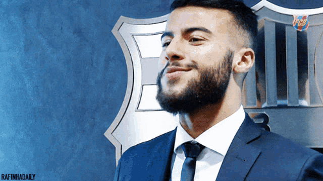 a man with a beard wearing a suit and tie is smiling in front of a fcb logo
