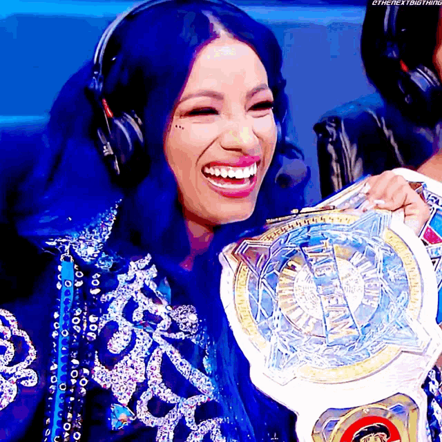 a woman with blue hair is smiling while holding a championship belt