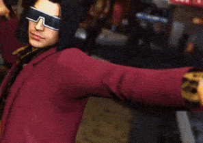 a man wearing sunglasses and a red jacket is standing in a street .