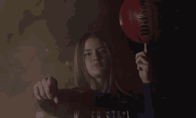 a woman holding a red wilson basketball pointing at the camera