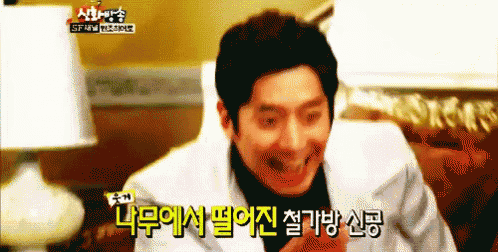 a man in a white suit and black turtleneck is laughing in a room with korean writing on the bottom