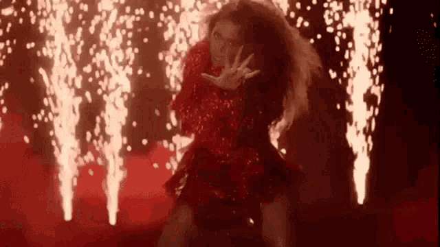 a woman in a red dress is dancing in front of fireworks in the dark .
