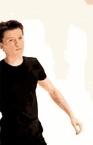 a young man in a black t-shirt is standing in front of a white wall with his arms outstretched .