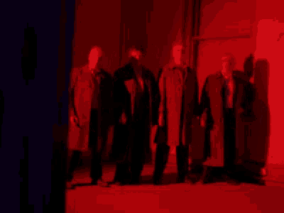 a group of men standing next to each other in a dark room with a red light behind them