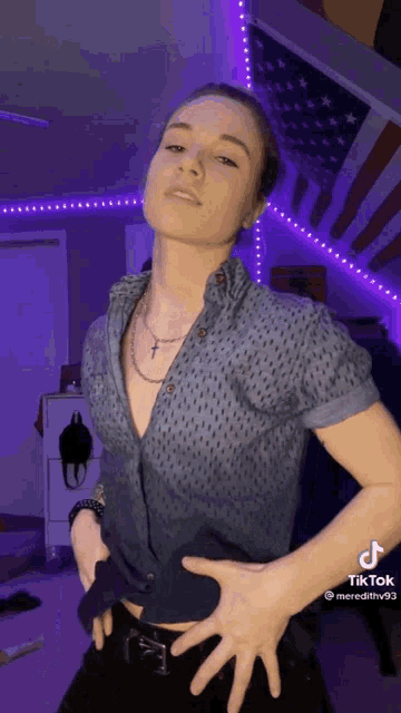 a woman in a blue shirt is dancing in front of a purple lighted wall