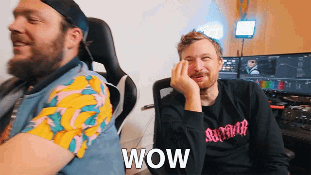 two men are sitting next to each other and one of them is wearing a shirt with the word wow on it