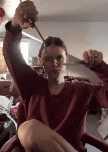 a woman in a red sweater is holding a pair of scissors above her head