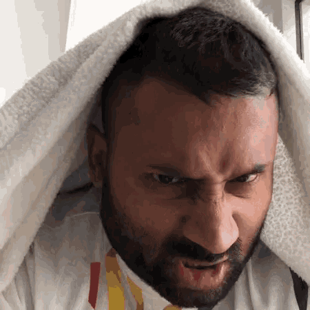 a man with a beard is making a funny face with a towel over his head .